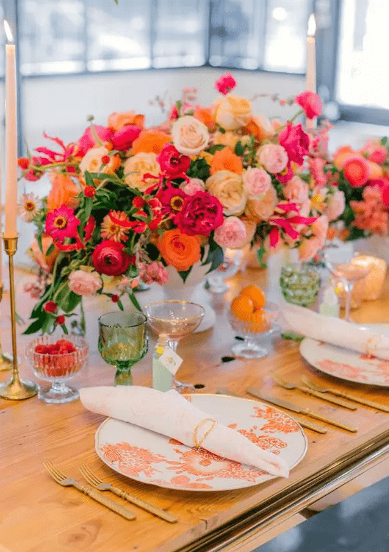 a pretty and bold tablescape with a bold floral centerpiece, hot pink, orange and pale pink blooms, florla print plates and colored glasses