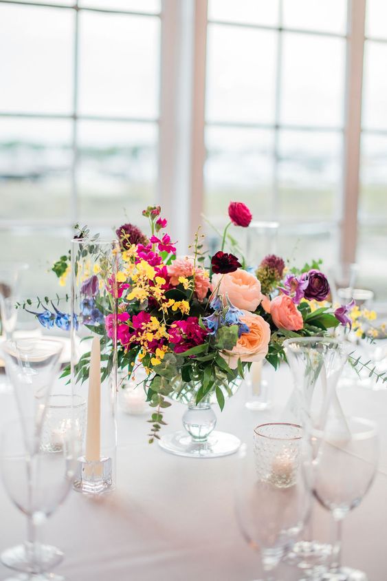 a pretty bright summer wedding centerpiece that consists of blush, yellow, fuchsia, blue and purple blooms and greenery