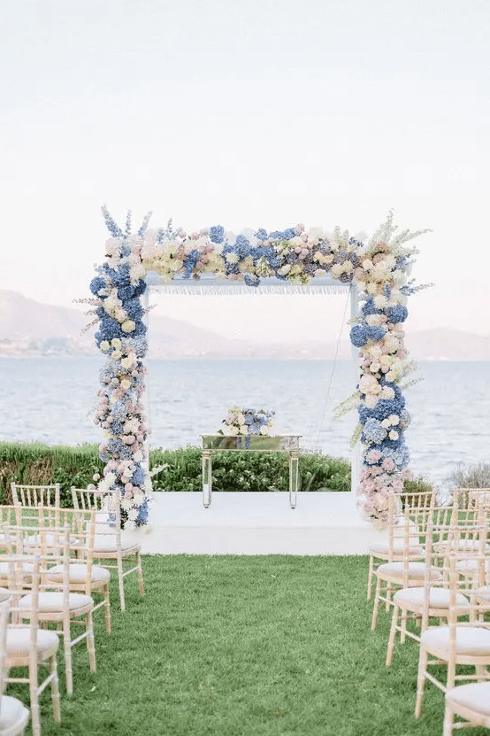 a pretty pastel wedding arch with white, blush and blue hydrangeas, deliphinium plus a cool sea view