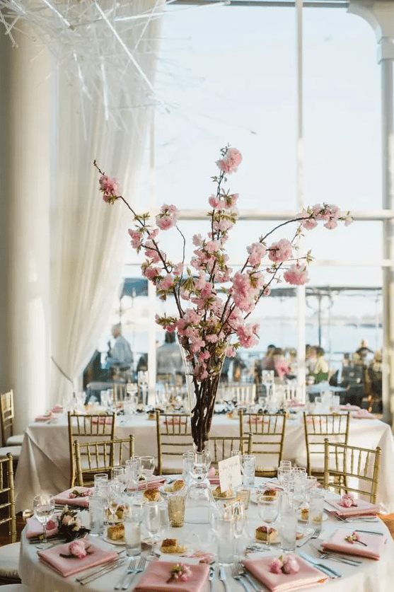 a pretty spring wedding tablescape with pink cherry blossom as a centerpiece, pink napkins and blooms and amber glasses