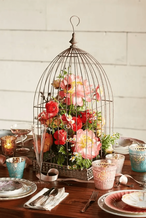 a pretty stylized birdcage with bright coral and pink blooms and greenery is a catchy idea for a wedding