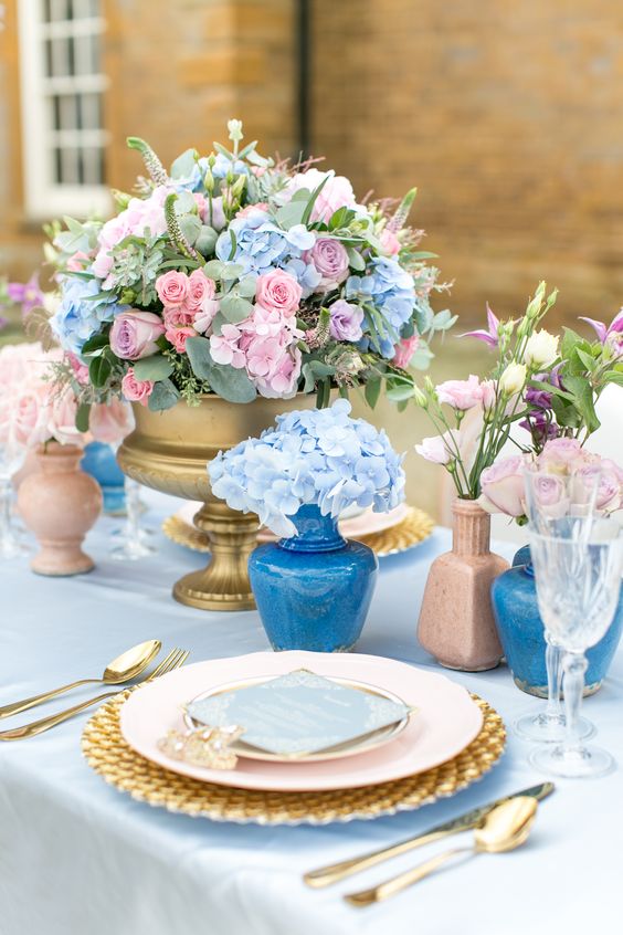 a refined pastel wedding centerpiece of a gold bowl with pastel pink, blue and purple blooms and greenery is amazing for spring