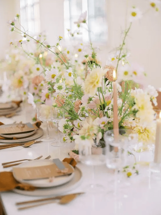 A sophisticated spring wedding tablescape with white, blush and yellow blooms, pink candles, rust colored napkins