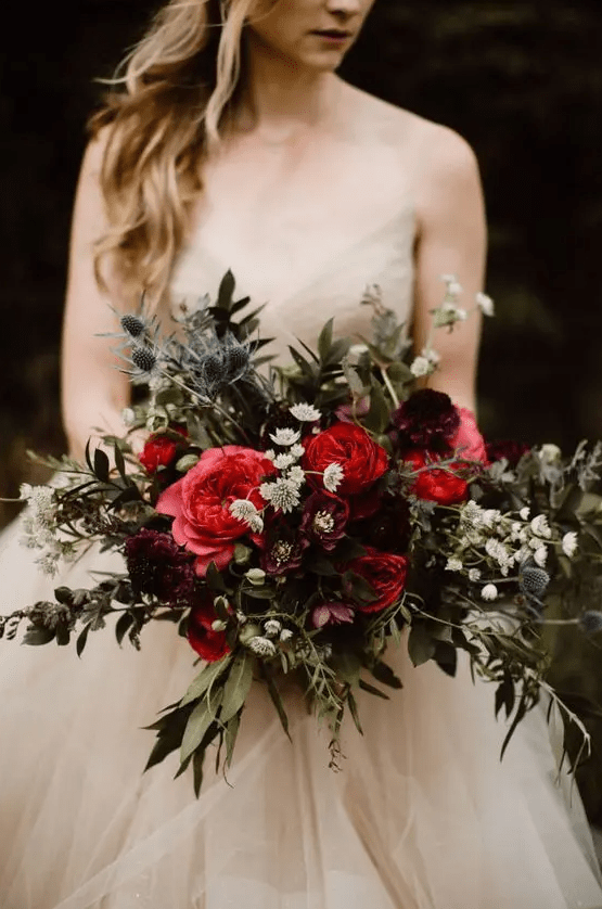a stunning moody fall wedding bouquet of depe red, pink, purple and white blooms, greenery and thistles is a gorgeous idea for a moody wedding