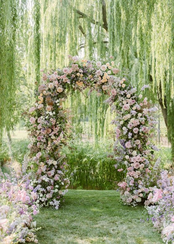 a subtle pastel wedding arch decorated with greenery, blush and dusty pink and peachy roses plus matching arrangements along the aisle
