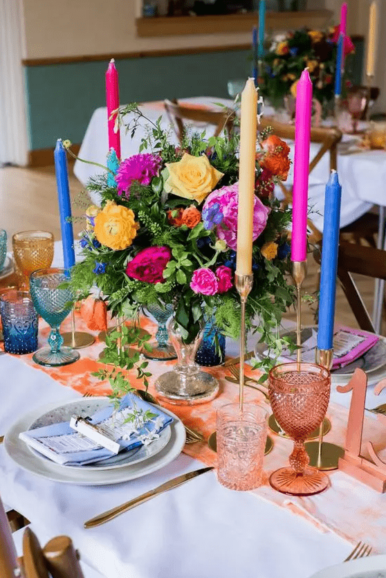 a sumptuous wedding tablescape with a peachy runner, glasses and a table number, navy, fuchsia candles, yellow and hot pink blooms