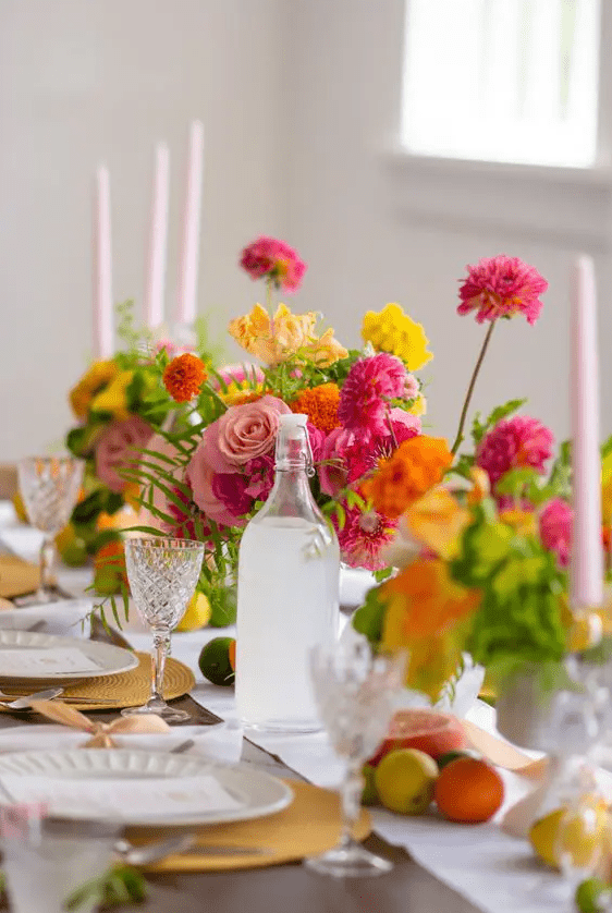 a super bright citrus-inspired wedding tablescape with hot pink, pink and yellow blooms, real citrus on the table and yellow placemats