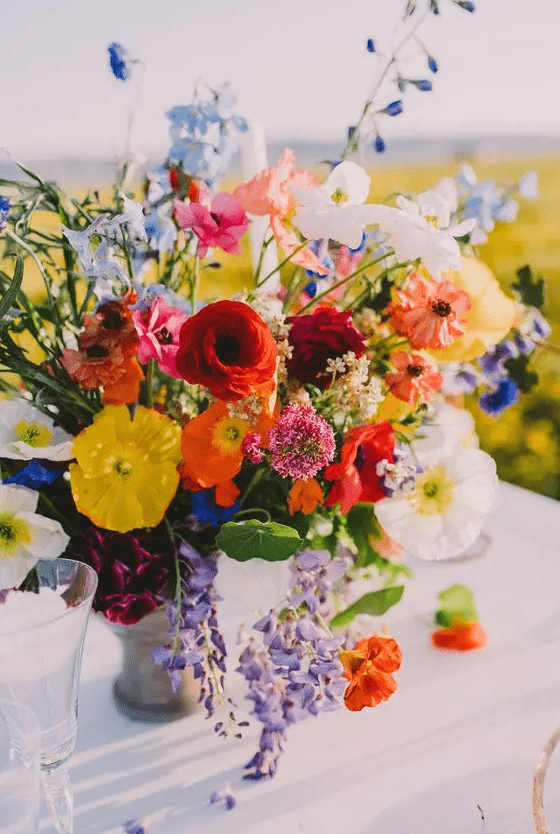 a super bright rustic wedding centerpiece of red, orange, yellow poppes, ranunculus, blue fillers and greenery is amazing