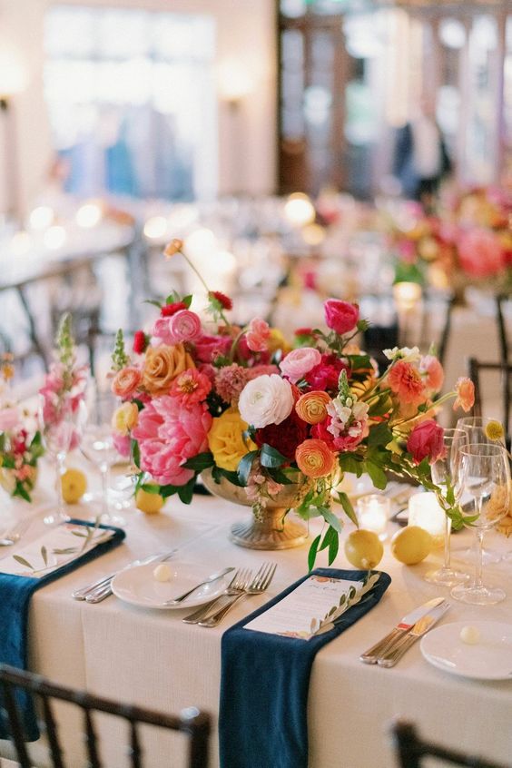 a vibrant wedding centerpiece of yellow, orange, coral, hot pink and pale pink blooms and lemons on the table