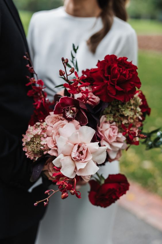 an eye-catchy wedding bouquet of burgundy roses and purple orchids, blush roses and hydrangeas for a dramatic look