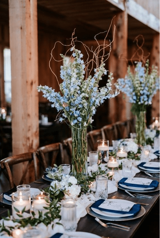an indoor spring wedding reception with pastel blue centerpieces and runners of greenery and white blooms and candles