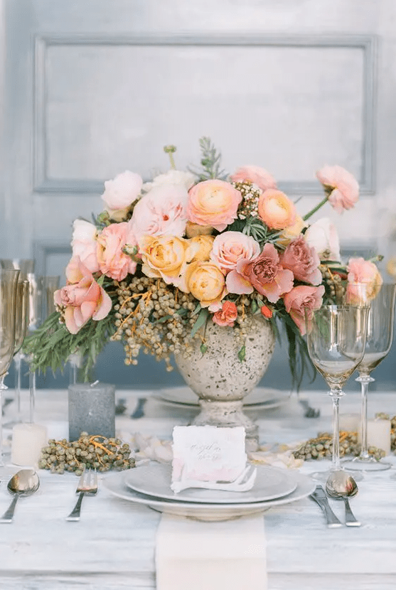 an ombre floral centerpiece with pink, mauve and yellow blooms, greenery and berries is a great idea for a spring or summer wedding