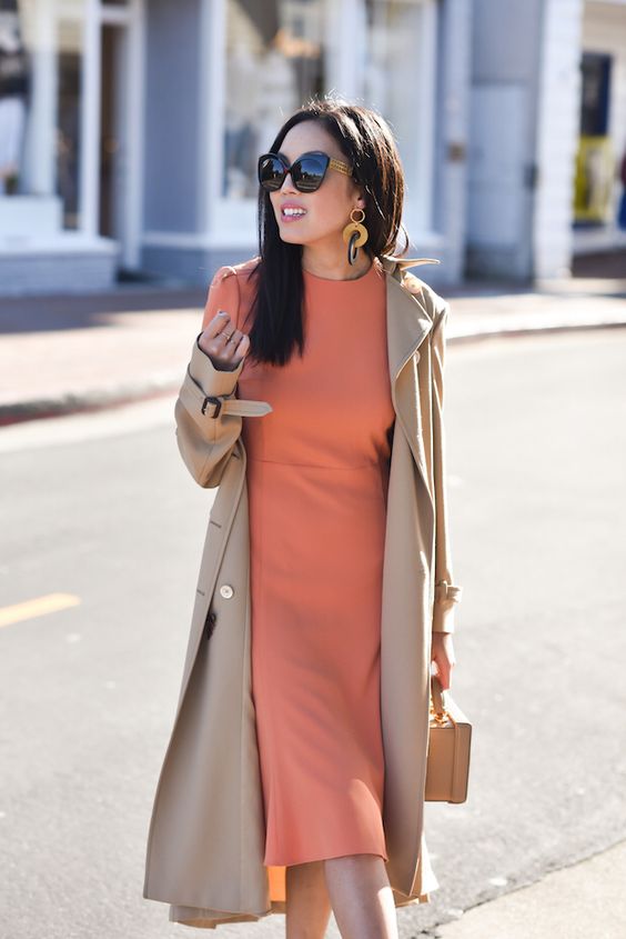 an orange midi dress, a tan trench, a tan box bag and statement earrings for a simple and cute sprign bridal shower look