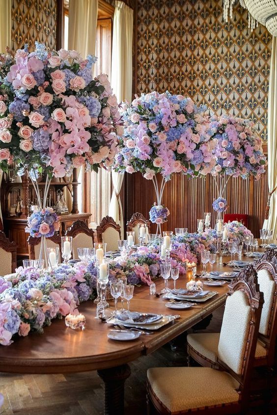 super lush and refined wedding centerpiece of pastel pink, peachy and blue blooms and a matching table runner on the table