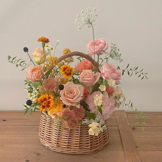 a basket summer wedding centerpiece of pink roses, rust marigolds, greenery and some fillers is amazing