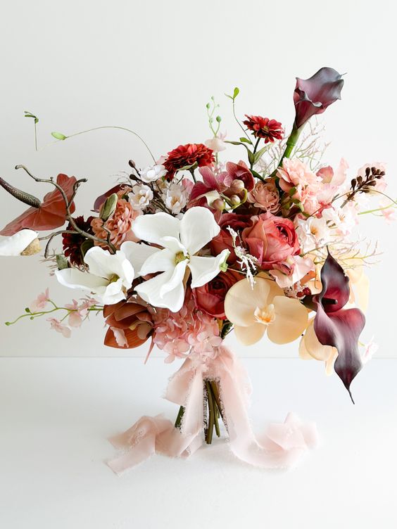 a beautiful and bold weddding bouquet of white and peachy orchids, deep purple callas and red blooms plus some twigs for the fall