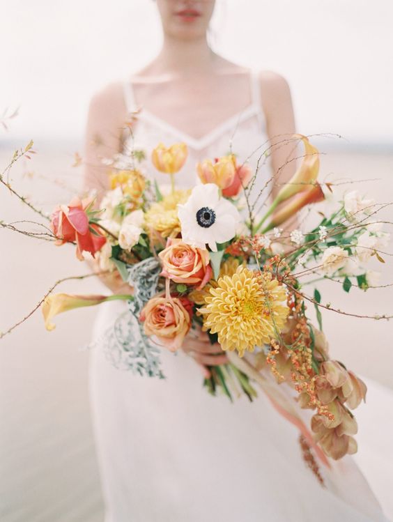 a beautiful fall wedding bouquet of orange roses, callas, tulips, anemones, some foliage and twigs is adorable