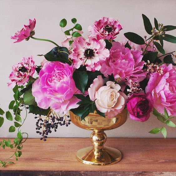 a beautiful wedding centerpiece of a gold bowl, pink peonies, anemones and roses and privet berries and greenery
