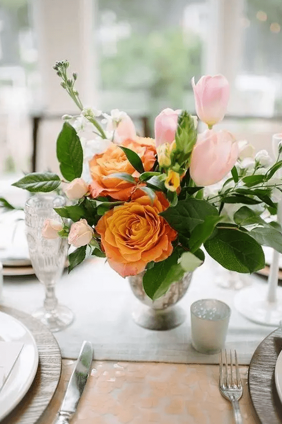 a beautiful wedding centerpiece of light pink tulips and roses, orange roses and greenery and candles around is wow