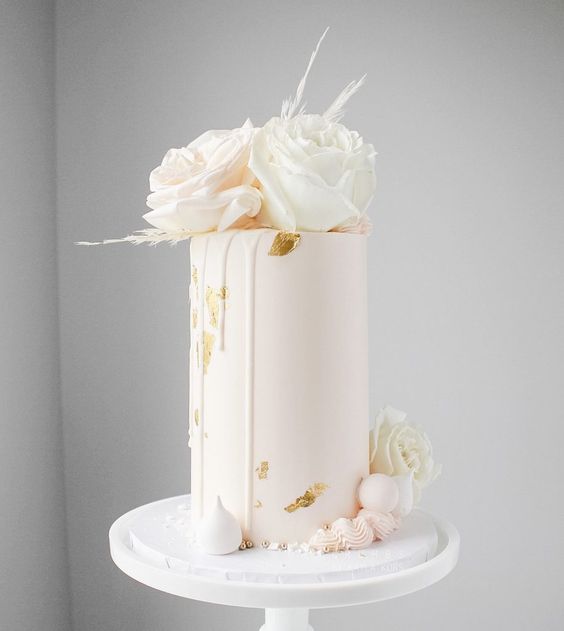 a blush tall wedding cake with gold leaf, white roses and grass and soem meringues at the bottom of the cake