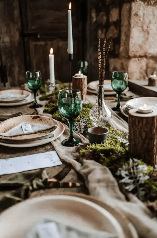 a boho wedding tablescape with a greenery and moss runner, candles, tree branches, feathers and tall and thin candles