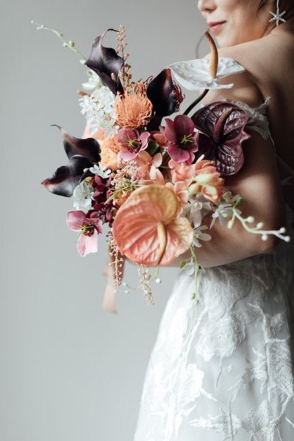 a bold fall wedding bouquet of deep purple callas, anthurium, orange and purple fillers and some blooming branches