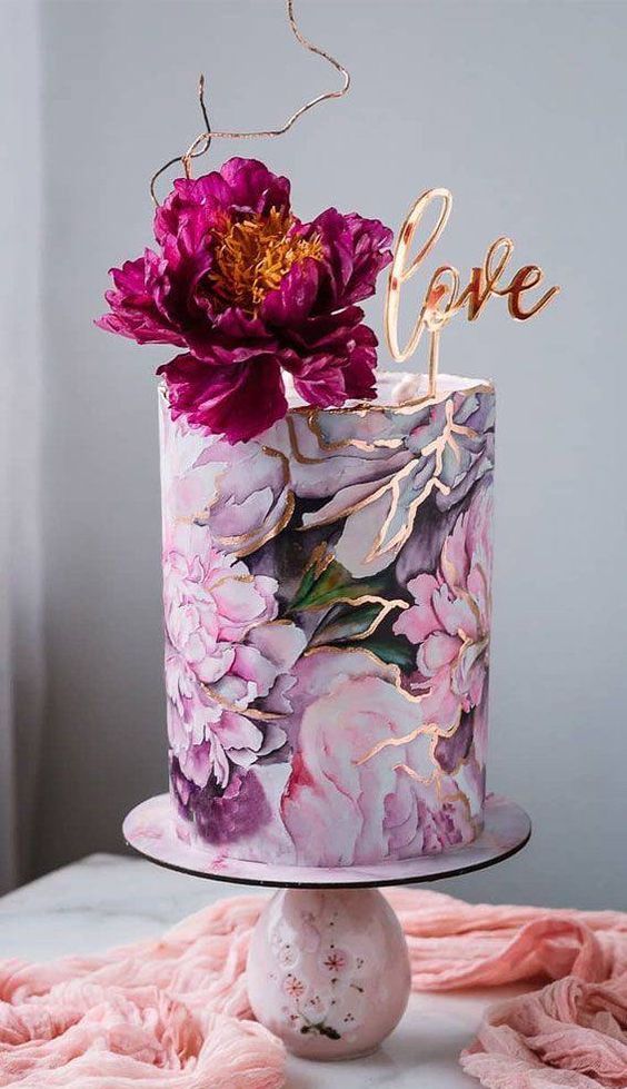 a bold pink floral paitned tall wedding cake with a gold calligraphy topper and a purple bloom on top
