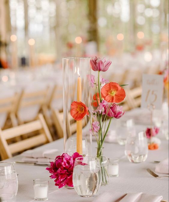 a bold wedding centerpiece of a peachy candle, hot pink tulips and a peony and orange poppies