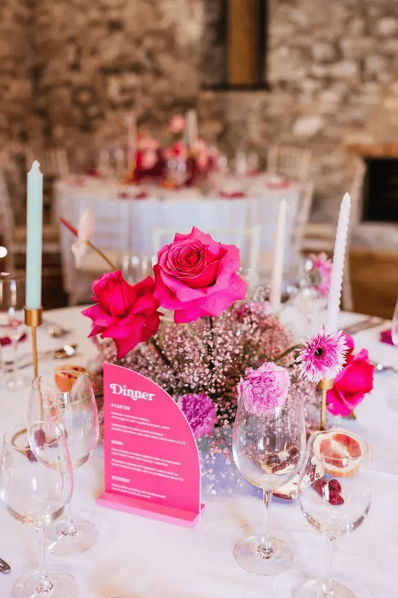 a bold wedding centerpiece of pink baby’s breath, hot pink roses and carnations and a pink menu next to it is a cool idea