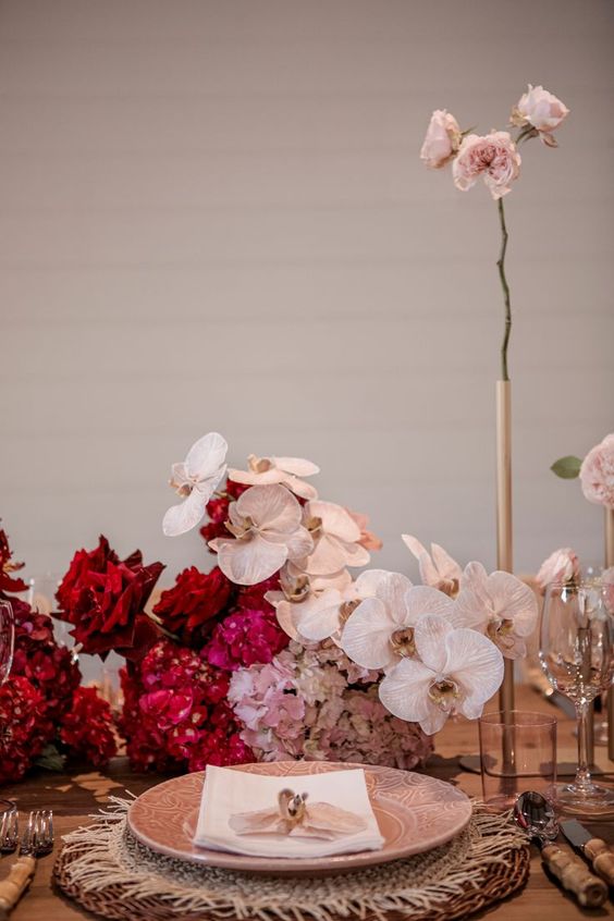 a bold wedding centerpiece of red roses, pink hydrangeas and blush orchids plus blush roses in a tube vase