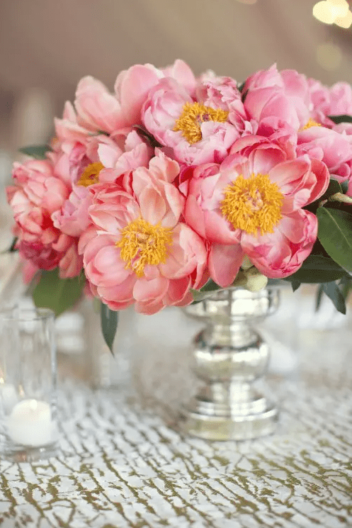 A bright vintage inspired summer wedding centerpiece of a silver vase and coral blooms with leaves is a lovely and bright idea