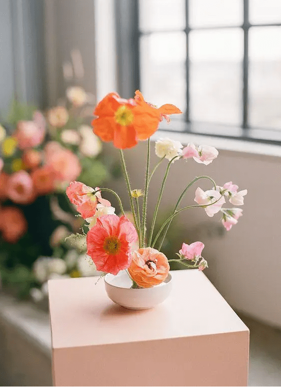 a catchy modern wedding centerpiece of coral, orange and light pink poppies, white and light pink blooms and greenery
