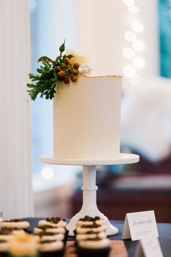 a chic sleek white wedding cake with a gilded edge, white blooms, berries and greenery is a cool idea