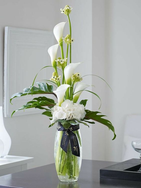 a chic wedding centerpiece of callas, monstera leaves and some fillers features a creative shape and looks modern