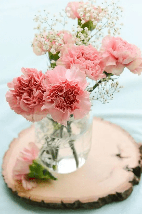 a chic wedding centerpiece of pink carnations and baby's breath plus a tree slice is a lovely idea for a rustic wedding
