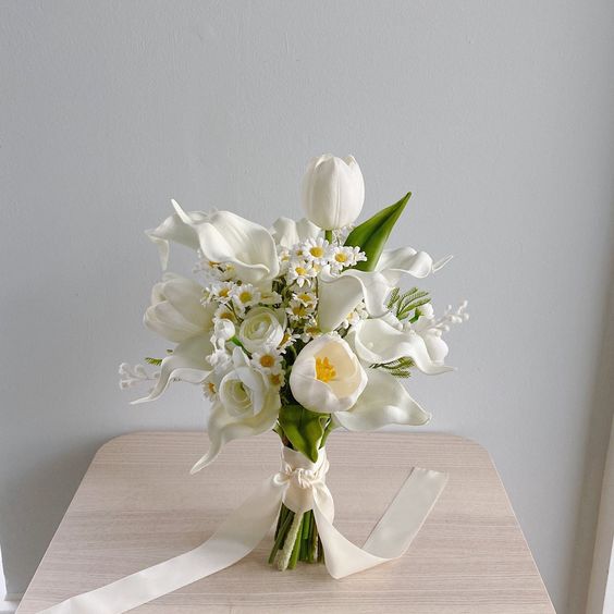 a chic white wedding bouquet of tulips, callas, roses and chamomiles plus some leaves