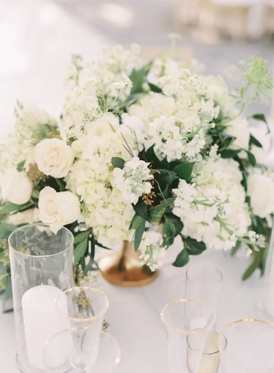 a classic wedding centerpiece of white roses and hydrangeas and greenery plus candles around is a cool idea for spring and summer