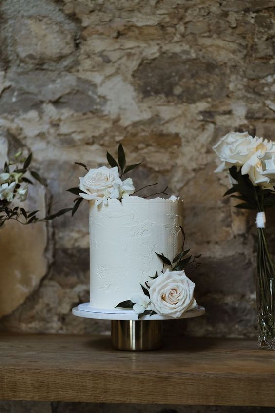 a classy modern tall white wedding cake with texture and white roses is a cool idea for any neutral wedding