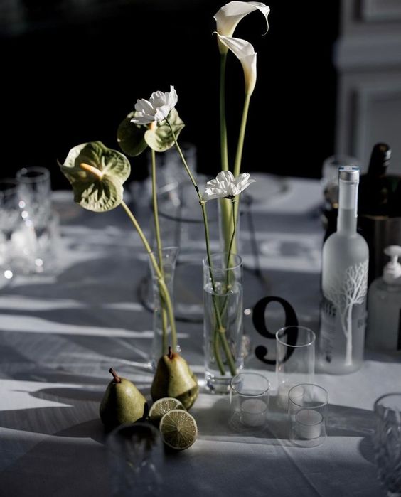 a cluster wedding centerpiece of anthurium, callas, white blooms in clear vases and fruit right on the table