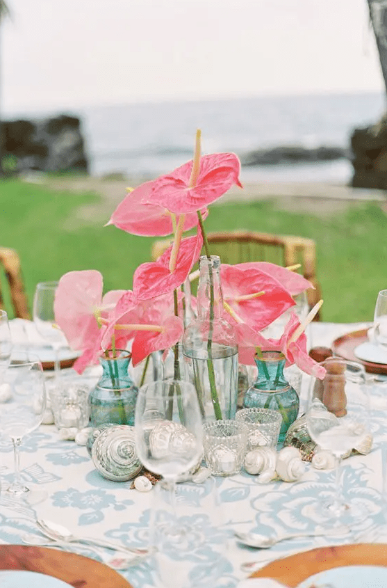 a cluster wedding centerpiece of coral anthurims and seashells on the table is a great idea for a beach wedding