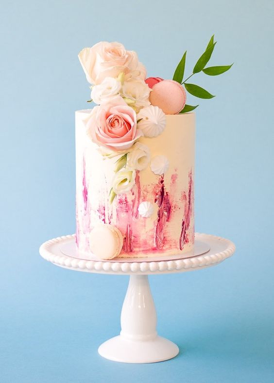 a colorful watercolor wedding cake with meringues, a pink macaron, blush roses and greenery