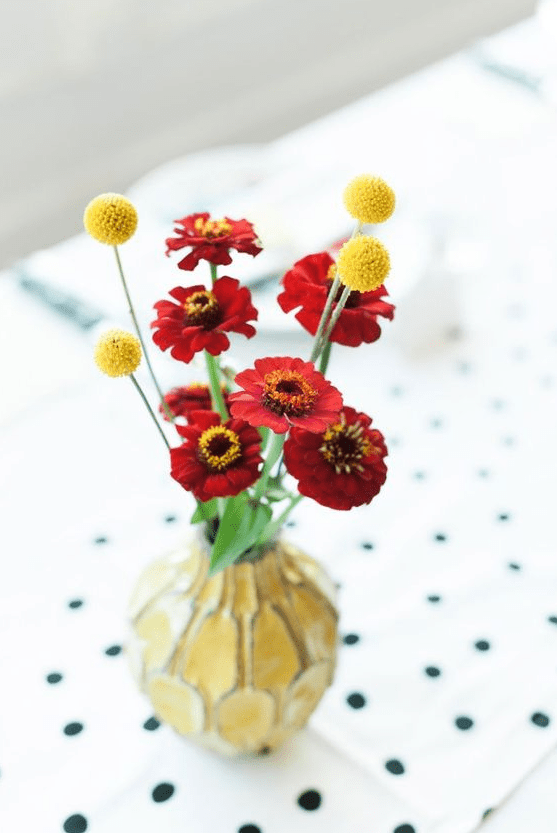 a colorful wedding centerpiece of bold red blooms and billy balls plus a catchy yellow vase for a summer or fall wedding