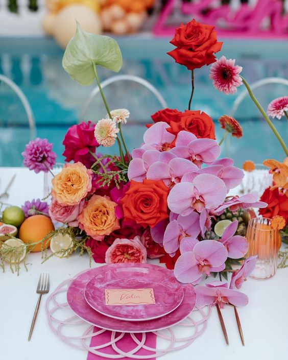 a colorful wedding centerpiece of hot pink and red roses, pink orchids, orange roses and pink mums, anthuriums and fruit on the table