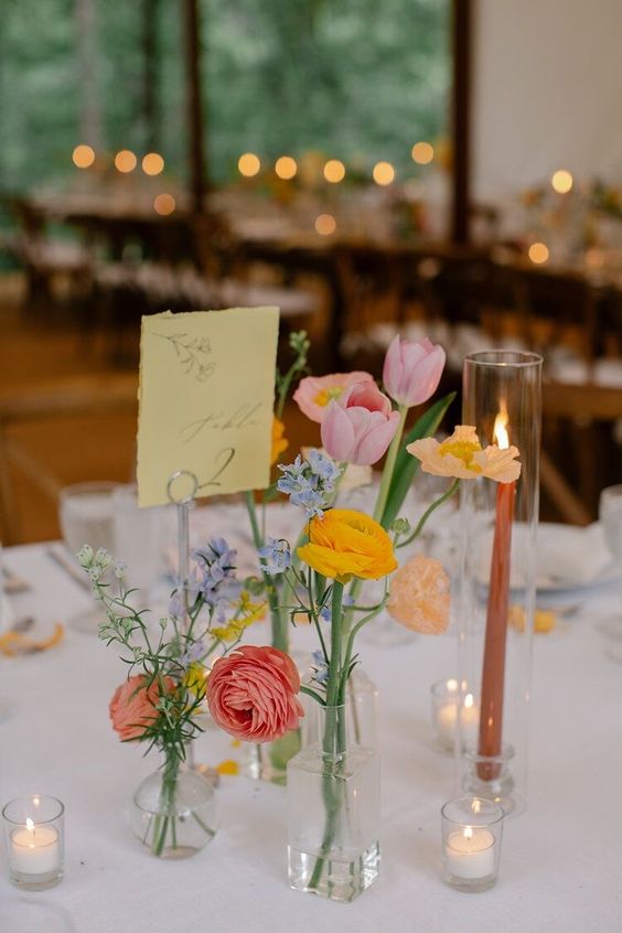a colorful wedding centerpiece of pink and yellow ranunculus, pink tulips and blue flowers is cool for spring or summer