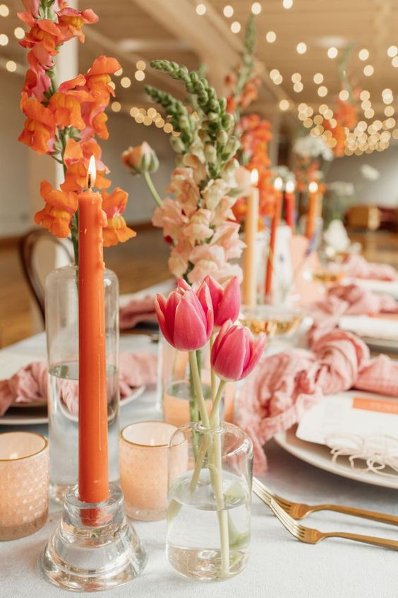 a colorful wedding centerpiece of pink tulips and orange blooms plus orange candles is a cool idea for summer