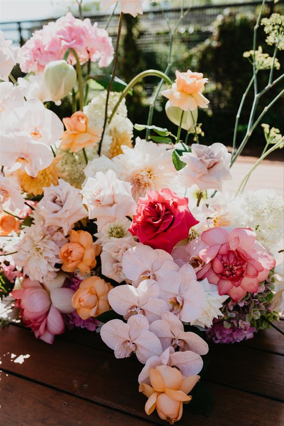 a colorful wedding centerpiece of red, pink, blush, orange roses, pale pink orchids and hydrangeas is very cool and chic