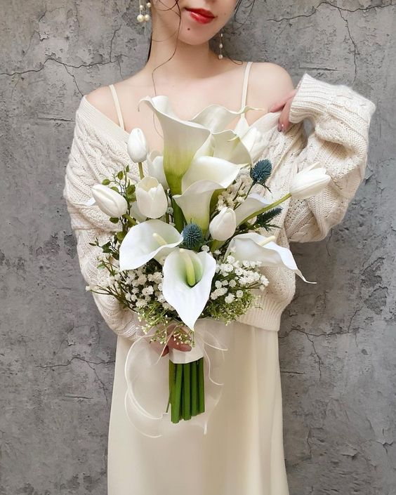 a cool modern wedding bouquet of baby's breath, callas, thistles, tulips, greenery and a wrap with a bow