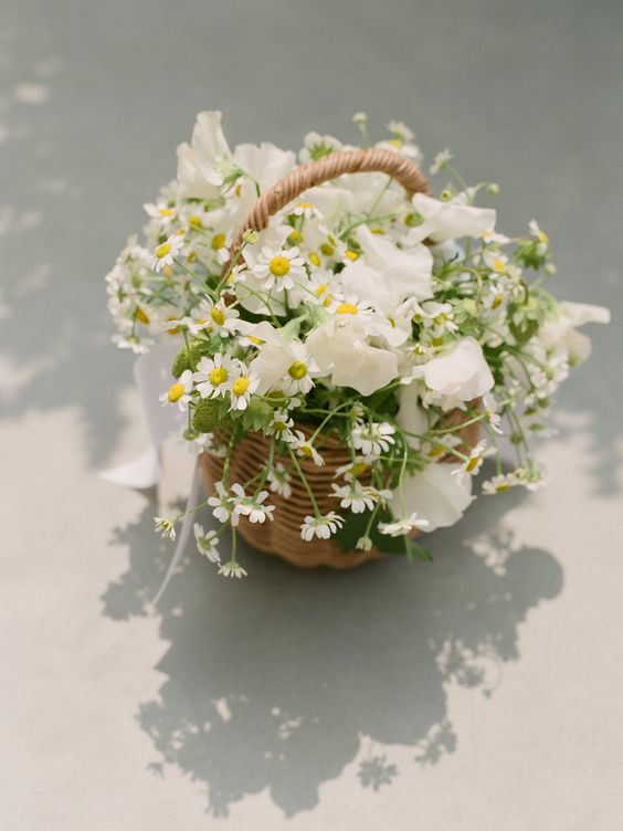 a cool summer wedding centerpiece of a basket with white sweet peas and chamomiles is a lovely idea