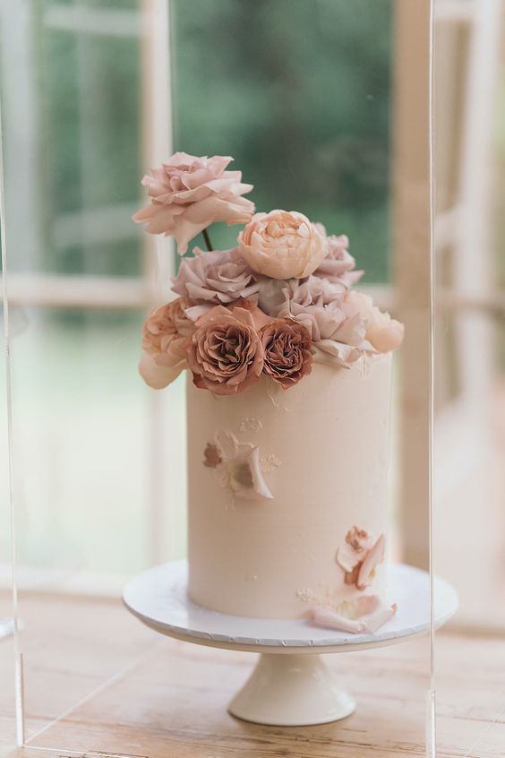 a delicate blush wedding cake with petals and blush and mauve roses on top is a lovely idea for spring
