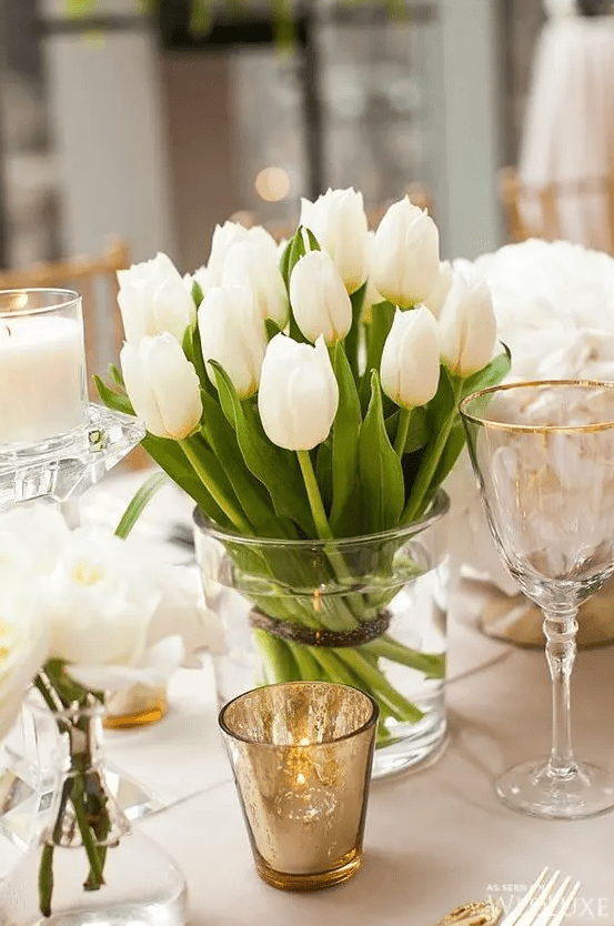 a delicate wedding centerpiece of white tulips, white roses and pillar candles is a chic idea for a spring wedding